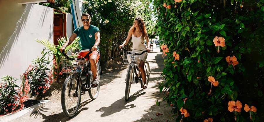 Leon und Sammy auf dem Fahrrad auf den Straßen von Caye Caulker neben einem Blumenbusch in Belize