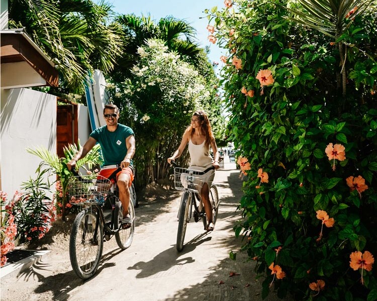 Leon und Sammy fahren auf dem Fahrrad durch die Straßen von Caye Caulker an einem sonnigen Tag neben schönen Blumen in Belize